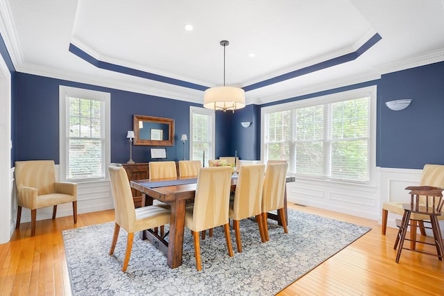 dining space featuring a raised ceiling, wainscoting, light wood-type flooring, and crown molding