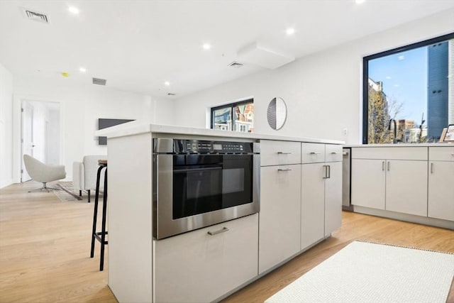 kitchen with light wood-type flooring, white cabinetry, oven, and a kitchen island