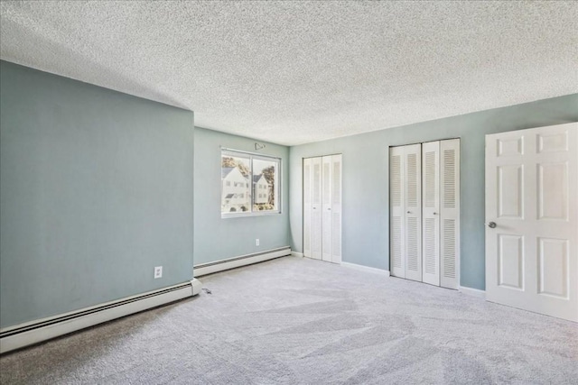 unfurnished bedroom with a textured ceiling, light colored carpet, baseboard heating, and multiple closets