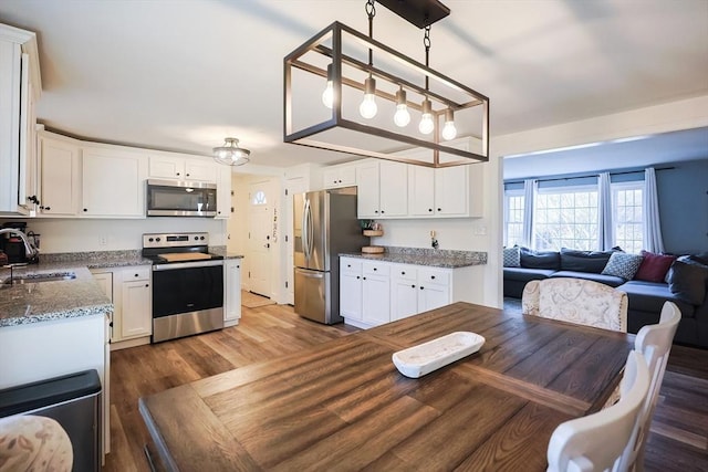 kitchen with a sink, white cabinets, open floor plan, and stainless steel appliances