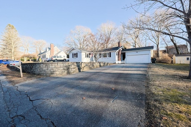 ranch-style home with aphalt driveway, a residential view, a garage, and a chimney