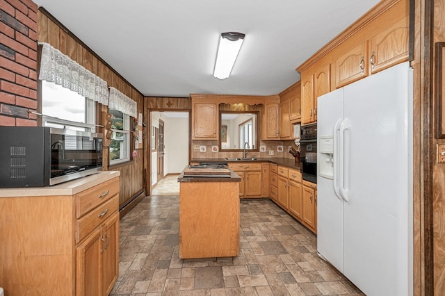 kitchen with oven, wooden walls, white refrigerator with ice dispenser, and a kitchen island