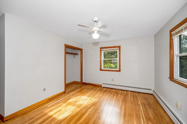 unfurnished bedroom featuring a closet, light hardwood / wood-style flooring, multiple windows, and a baseboard heating unit