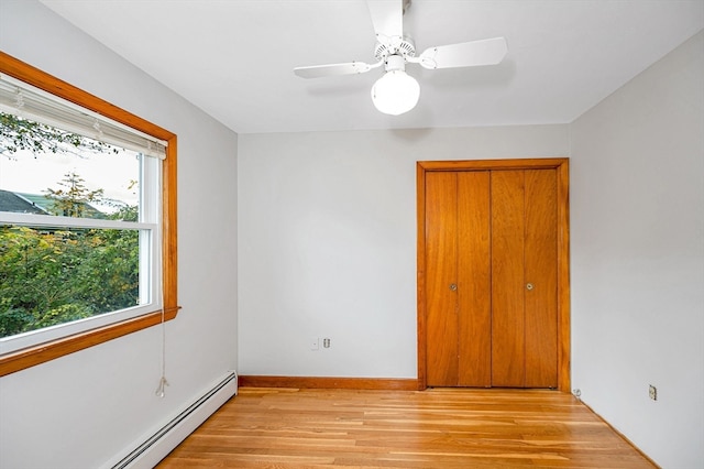 empty room featuring a wealth of natural light, a baseboard heating unit, light wood-type flooring, and ceiling fan