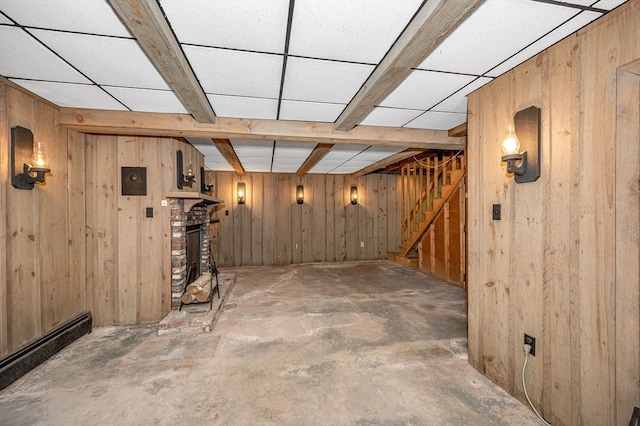 basement with wooden walls, a baseboard heating unit, a drop ceiling, and a fireplace