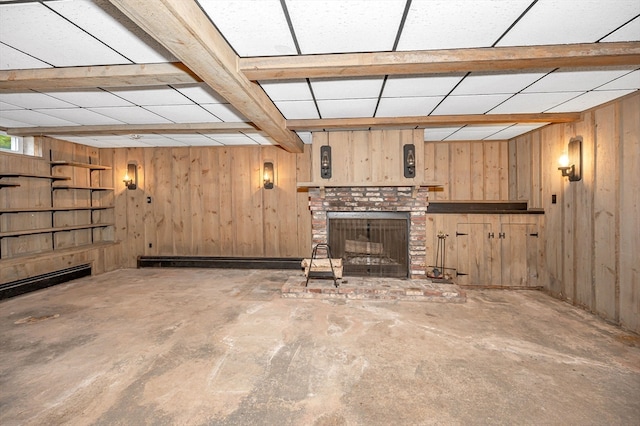 basement with wooden walls, a drop ceiling, and a fireplace