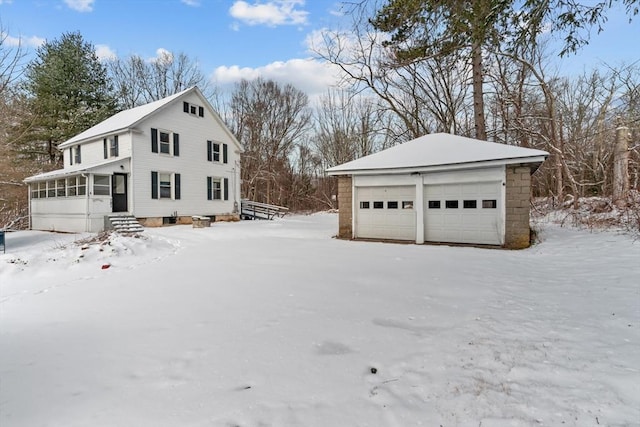 view of snow covered exterior with a garage, an outdoor structure, and a sunroom