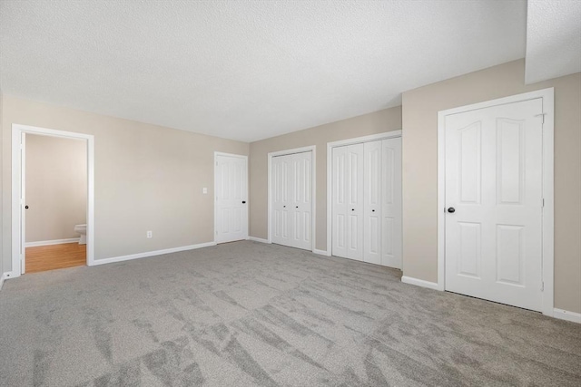 unfurnished bedroom with multiple closets, light carpet, connected bathroom, a textured ceiling, and baseboards