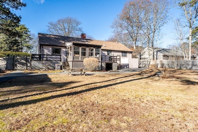 rear view of house with a wooden deck, a lawn, and a sunroom