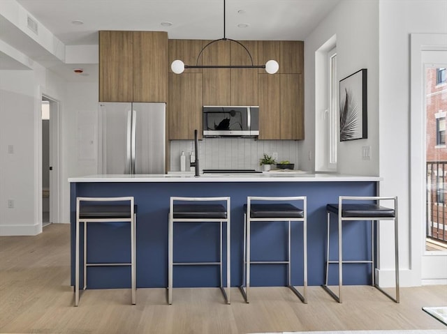 kitchen featuring light countertops, brown cabinetry, stainless steel appliances, light wood-style flooring, and decorative backsplash