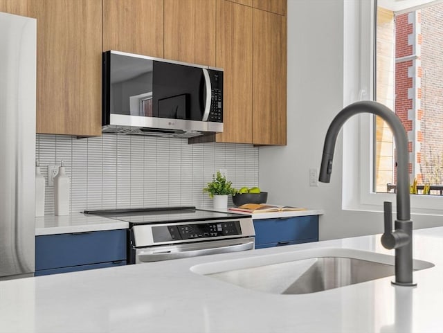 kitchen featuring modern cabinets, a sink, light countertops, stainless steel appliances, and backsplash