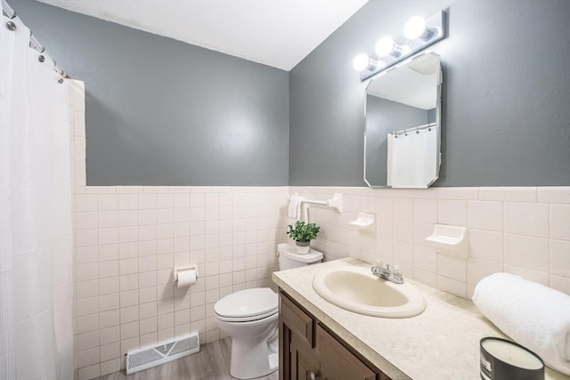 bathroom featuring vanity, wood finished floors, visible vents, tile walls, and toilet