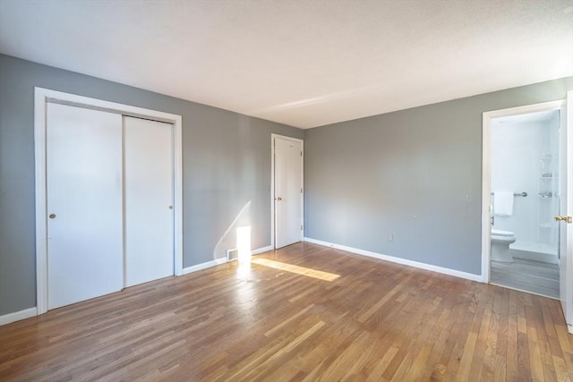 unfurnished bedroom featuring visible vents, wood finished floors, connected bathroom, a closet, and baseboards