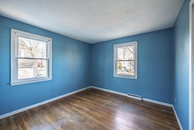 empty room featuring baseboards, baseboard heating, and hardwood / wood-style floors