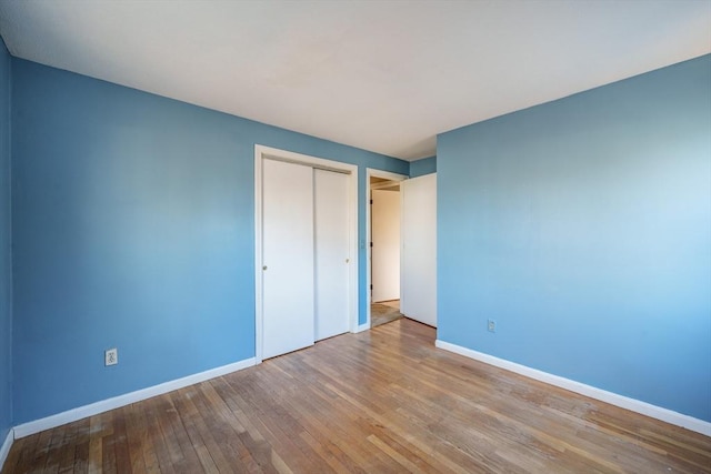 unfurnished bedroom featuring hardwood / wood-style flooring, baseboards, and a closet