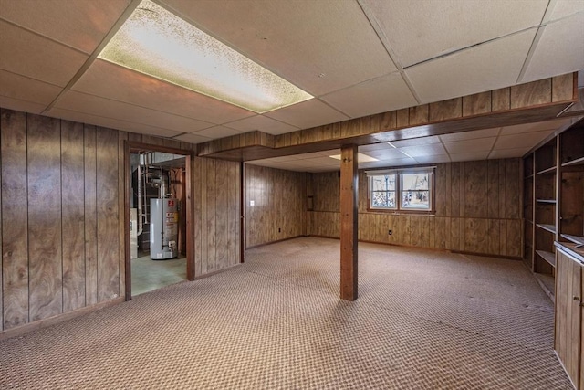 below grade area featuring carpet flooring, a paneled ceiling, water heater, and wood walls