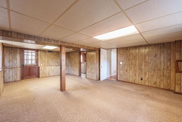 below grade area featuring carpet flooring, wood walls, washer / clothes dryer, and a paneled ceiling