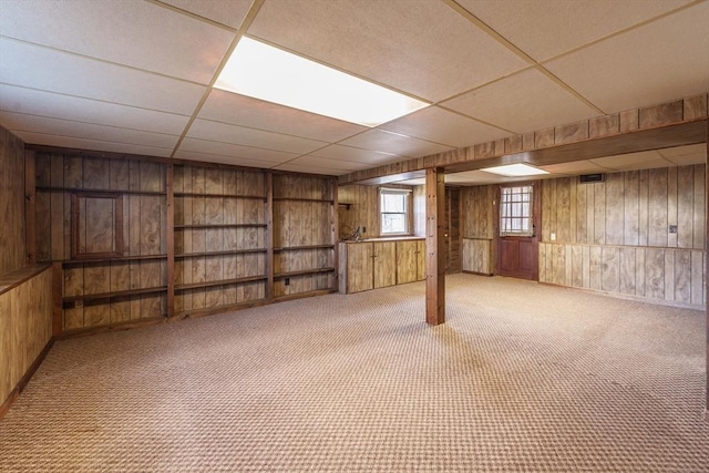 basement with wooden walls, a paneled ceiling, and carpet floors