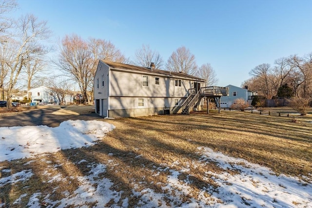 snow covered property featuring stairway, a garage, a wooden deck, and a chimney