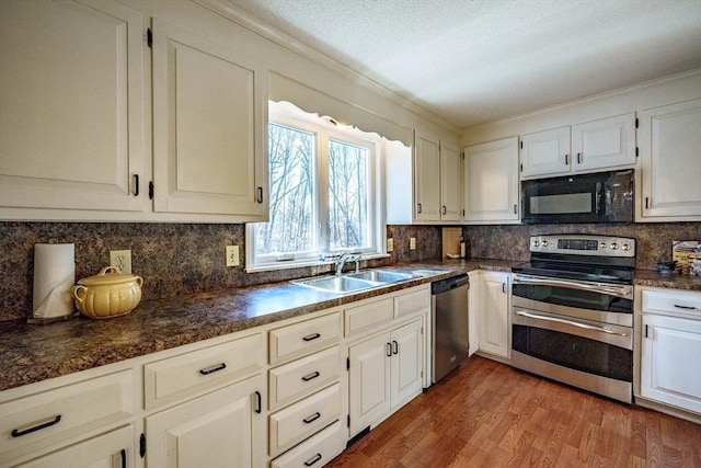 kitchen with wood finished floors, a sink, appliances with stainless steel finishes, dark countertops, and tasteful backsplash