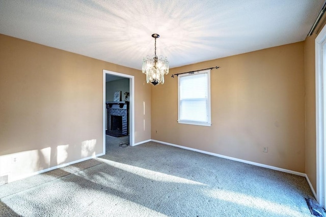 carpeted spare room featuring a notable chandelier, a fireplace, baseboards, and a textured ceiling