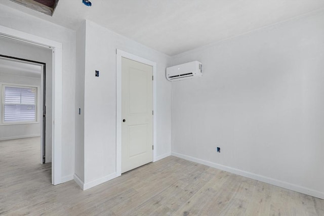 unfurnished bedroom with a wall unit AC and light hardwood / wood-style floors