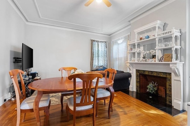 dining area with ornamental molding, a fireplace, ceiling fan, and wood finished floors