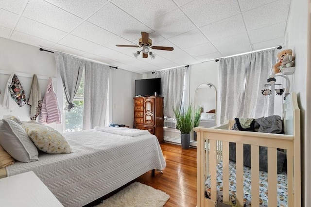 bedroom with ceiling fan, wood finished floors, and a paneled ceiling