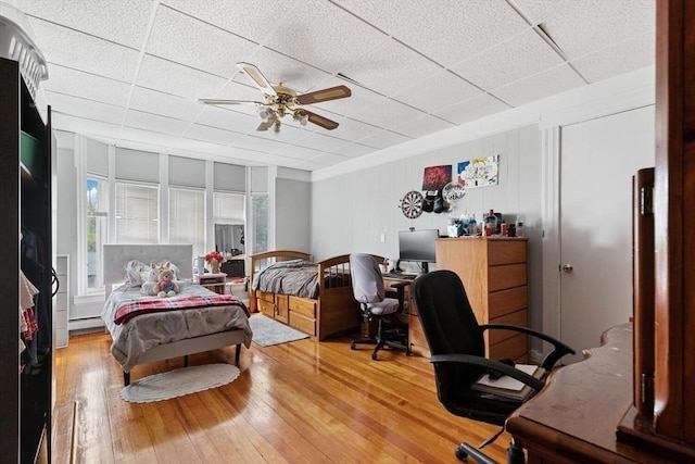 bedroom with a drop ceiling, wood-type flooring, baseboard heating, and a ceiling fan