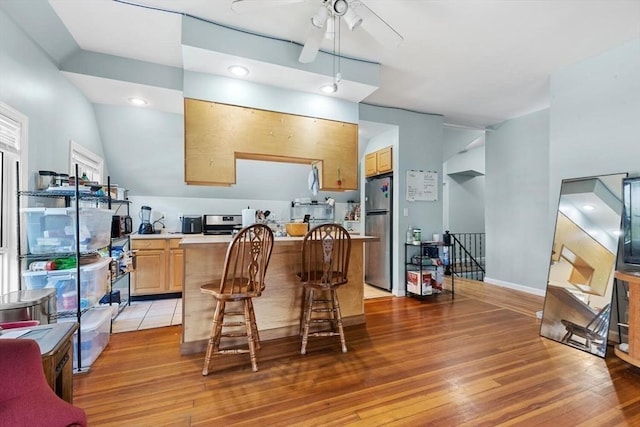 kitchen with light wood-style flooring, freestanding refrigerator, ceiling fan, light brown cabinetry, and light countertops