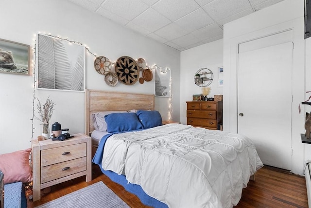 bedroom with a baseboard heating unit, a paneled ceiling, and wood finished floors