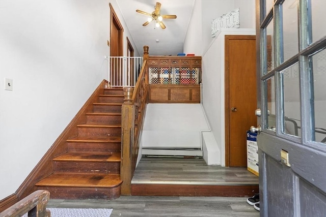 stairway with a baseboard heating unit, wood finished floors, and ceiling fan