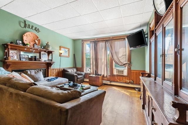 living room featuring baseboard heating, wainscoting, wood walls, and light wood-style floors