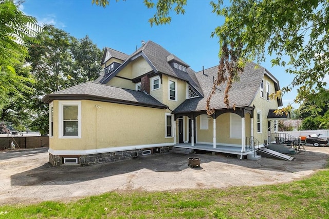 view of front facade with stucco siding, a porch, roof with shingles, and fence