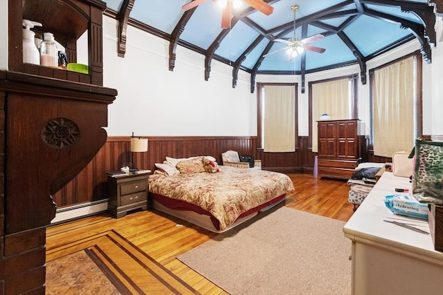 bedroom featuring a wainscoted wall, light wood-type flooring, a baseboard heating unit, and vaulted ceiling