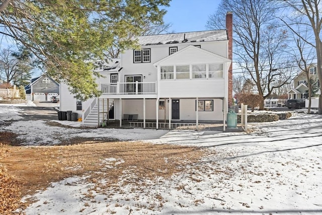 snow covered rear of property featuring a sunroom