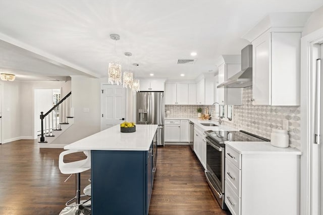 kitchen with stainless steel appliances, wall chimney range hood, a center island, and white cabinetry