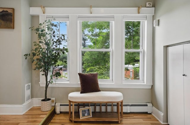 living area with healthy amount of natural light, baseboard heating, and wood finished floors