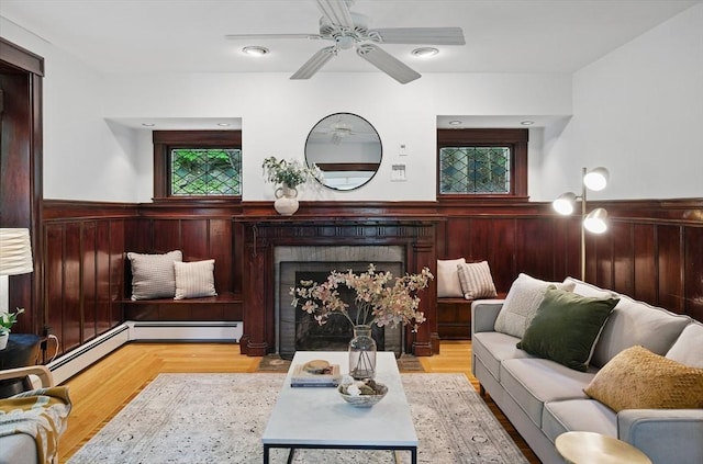 living area featuring wainscoting, a ceiling fan, a fireplace, wood walls, and wood finished floors