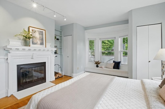 bedroom featuring track lighting, wood finished floors, a fireplace with flush hearth, and baseboards