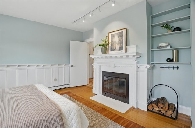bedroom featuring baseboard heating, a fireplace with flush hearth, wood finished floors, and track lighting