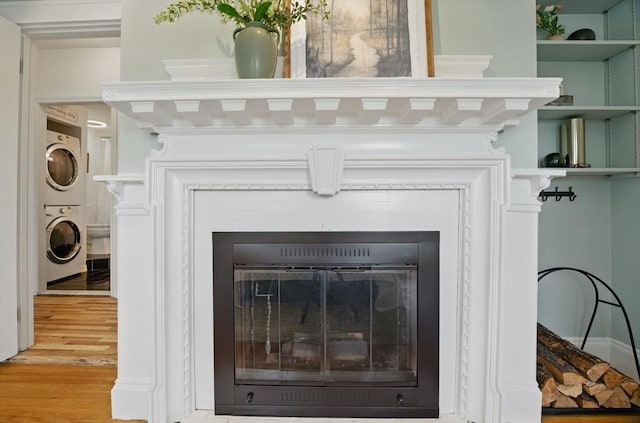 detailed view of stacked washer / dryer, wood finished floors, and a fireplace