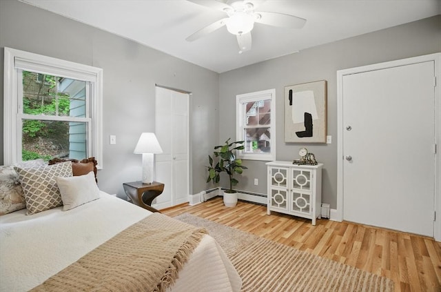 bedroom with light wood finished floors, ceiling fan, a baseboard radiator, and baseboards