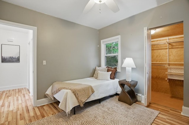 bedroom featuring light wood-style floors, ceiling fan, a baseboard heating unit, baseboards, and a spacious closet