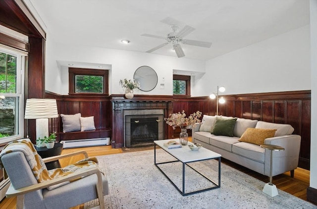 living area featuring a baseboard radiator, a brick fireplace, wood finished floors, and ceiling fan