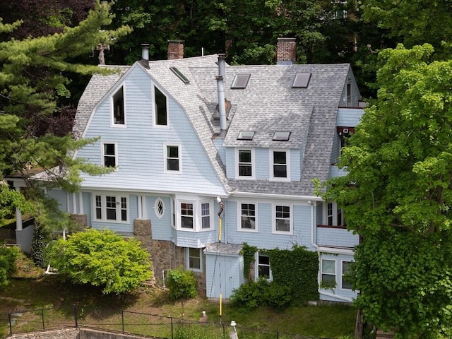 view of front of house with fence, a chimney, a gambrel roof, and a shingled roof