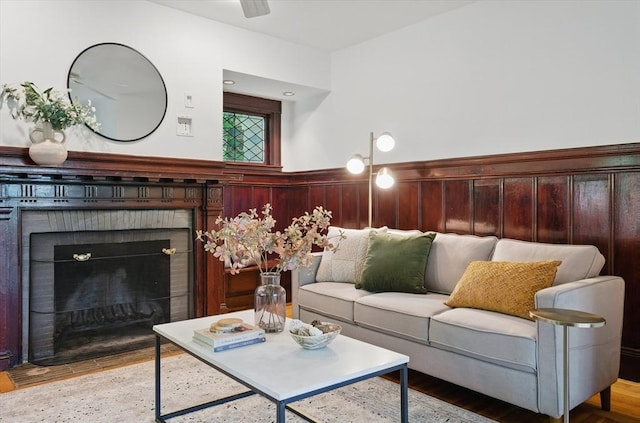 living room with wainscoting, wood finished floors, a fireplace, and a ceiling fan