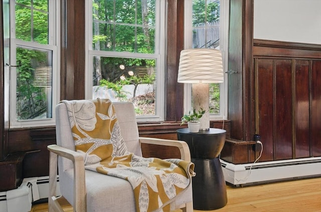 living area with a baseboard heating unit, healthy amount of natural light, and wood finished floors