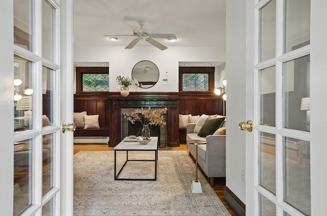 sitting room featuring french doors, a baseboard radiator, wood finished floors, and a ceiling fan