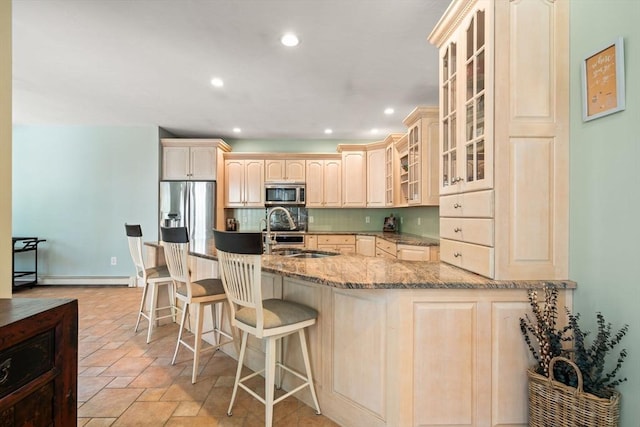 kitchen featuring a kitchen bar, appliances with stainless steel finishes, light stone countertops, baseboard heating, and a sink